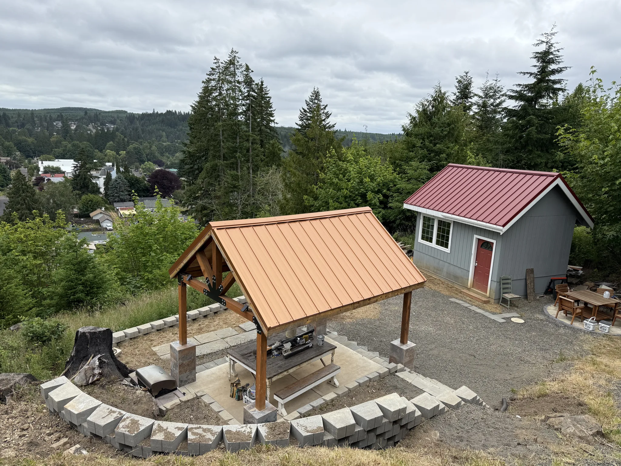 The finished tiny house and the timber pavilion on the hillside, the stone terrace between them